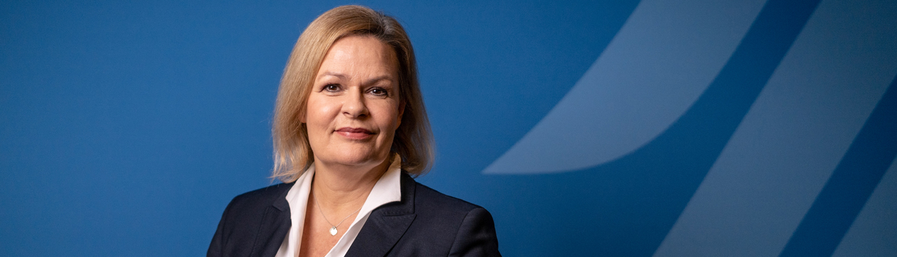 Portraitfoto von Bundesinnenministerin Nancy Faeser vor einer blauen Wand