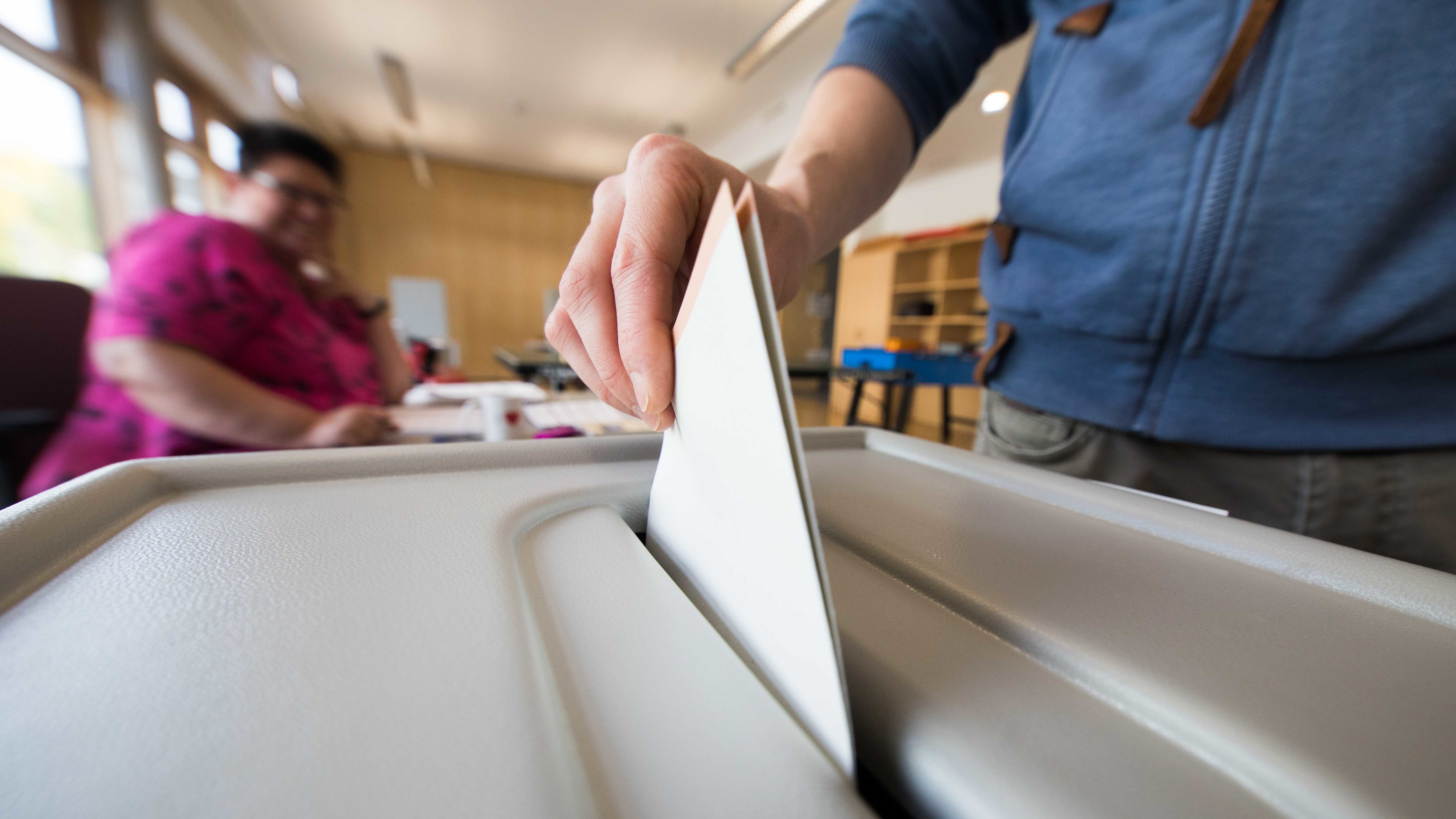 A hand throwing a ballot in a ballot box